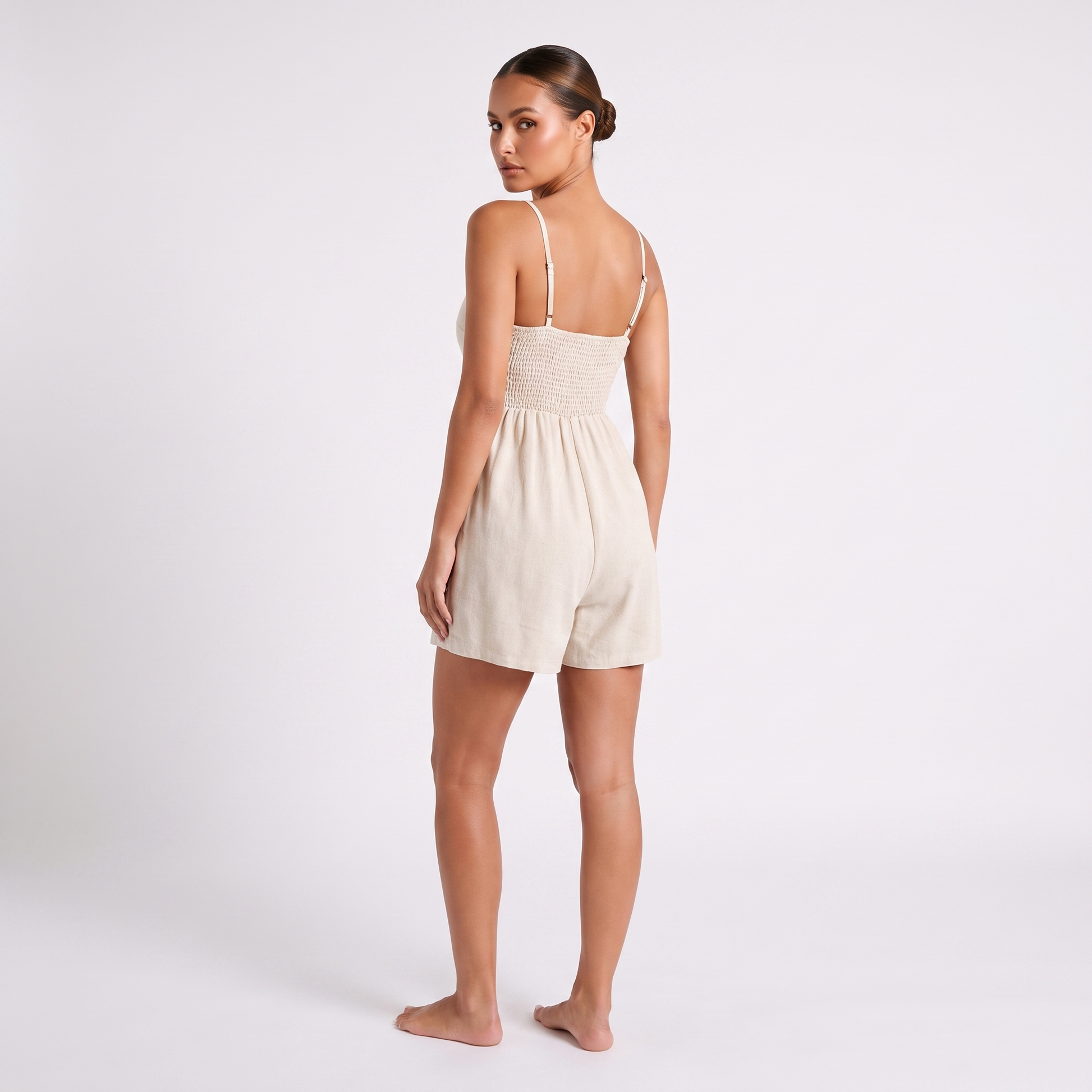 Casual Linen Romper in Apricot oatmeal linen - full length back view showing the shirred smocked elasticated back panel, both straps meeting its top edge and the self-fabric adjustable slider on each strap.