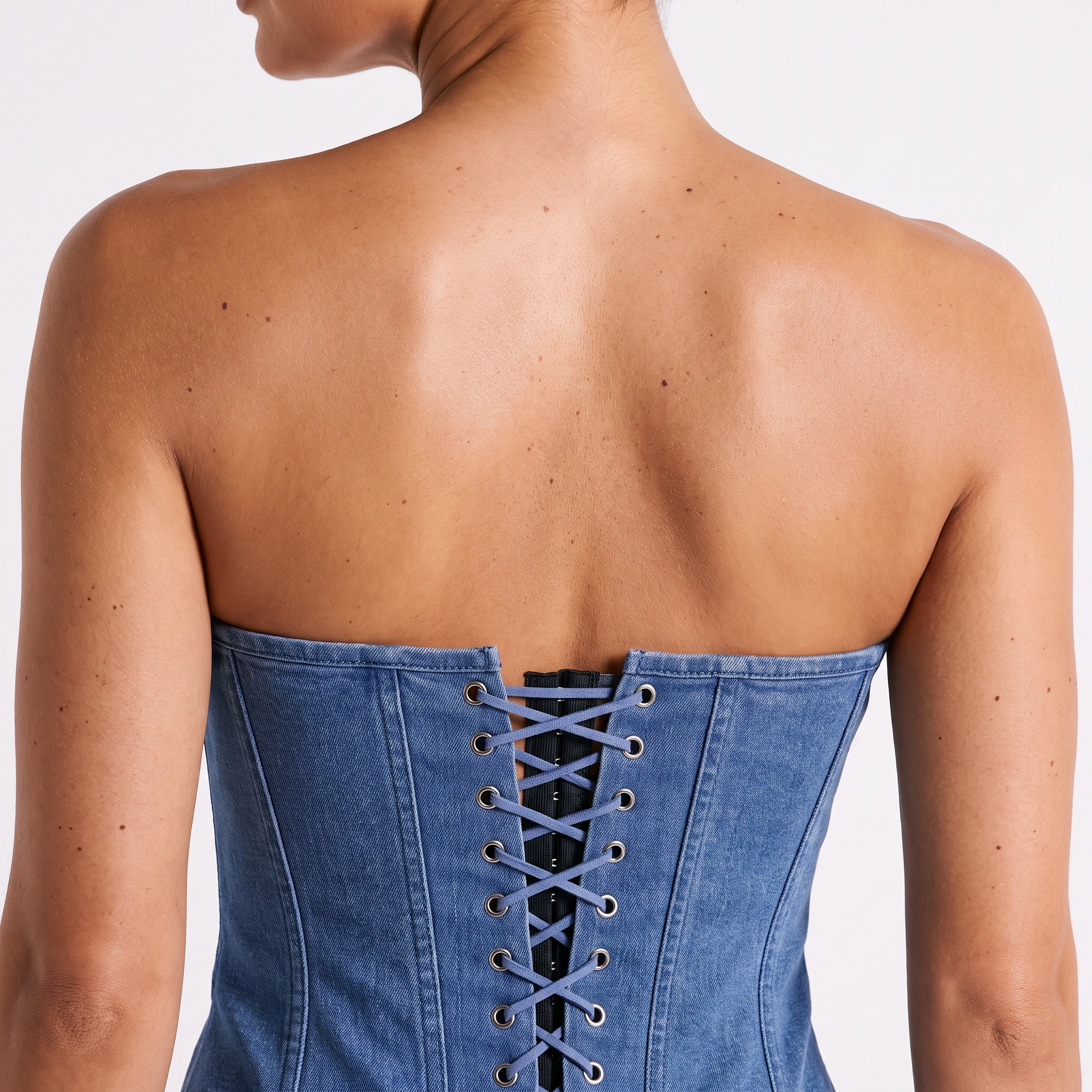 Denim corset vest back detail — centre-back lace-up with silver eyelets and denim-blue criss-cross cord